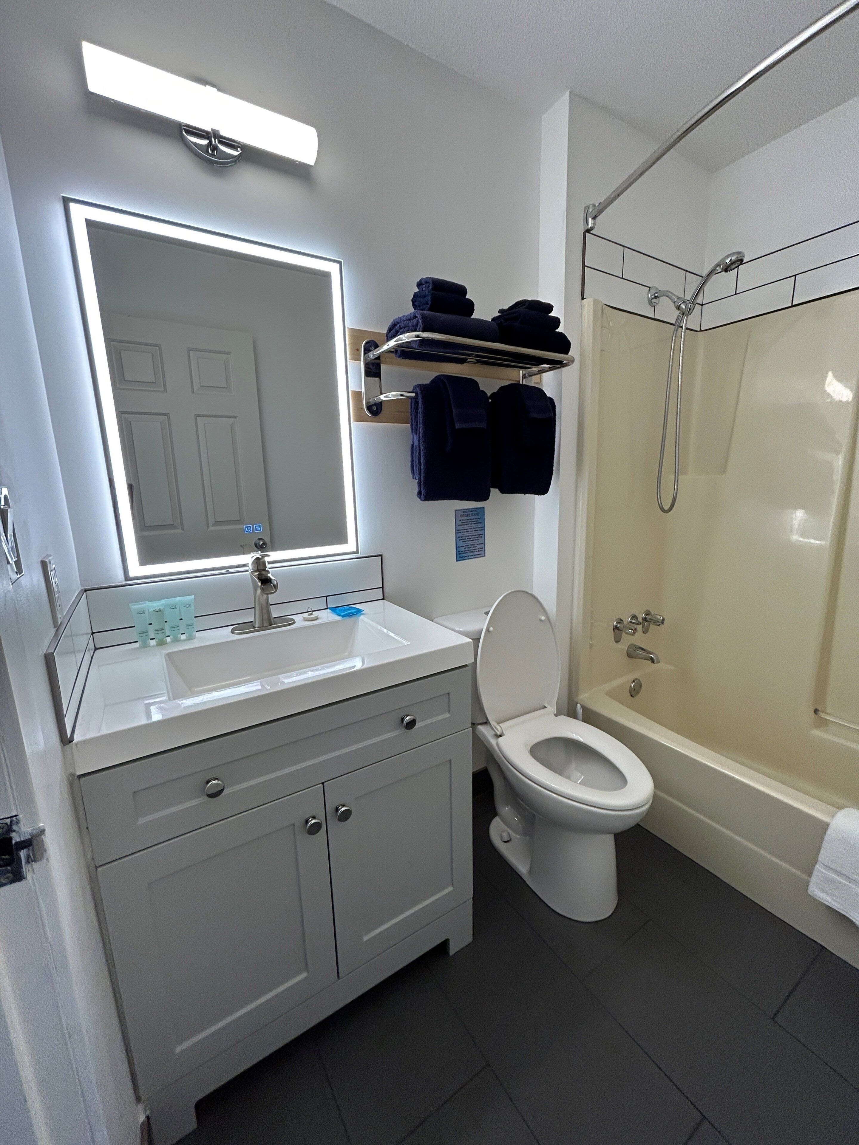 A bathroom with a white sink, mirror, toilet, and shower. There are towels and toiletries on the wall.
