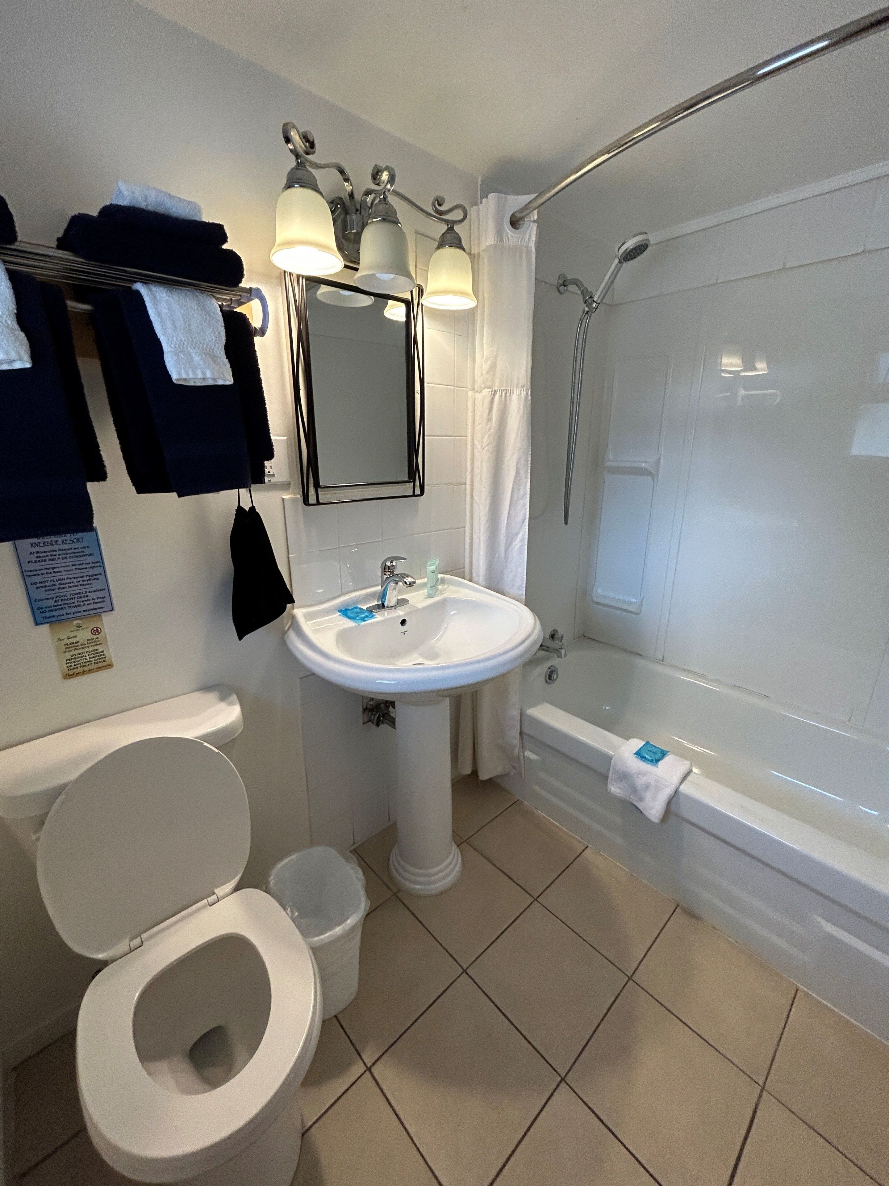 Un baño con inodoro, lavamanos y bañera. Hay toallas colgadas en la pared y una cortina de ducha.