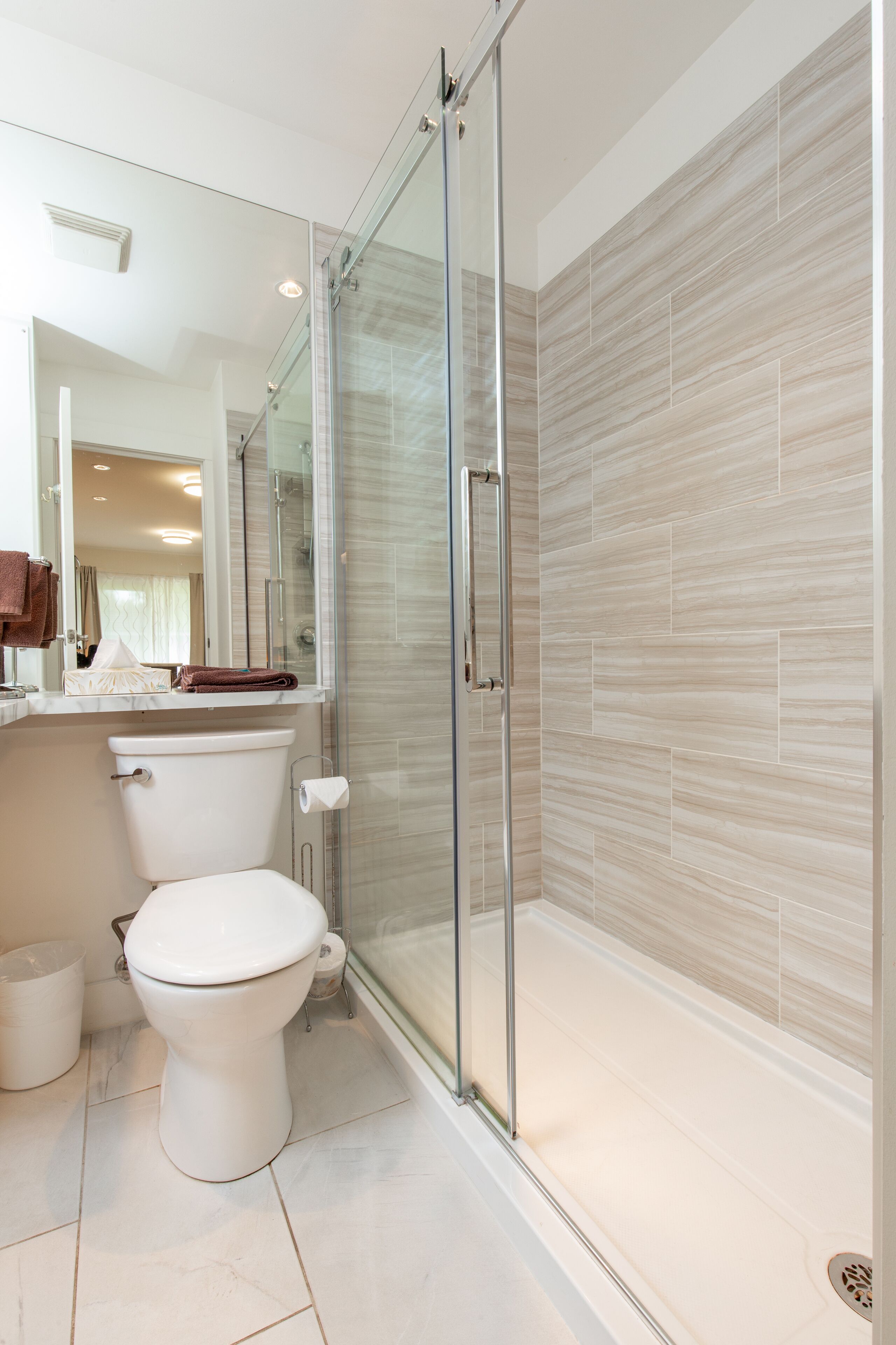 A modern bathroom with a glass shower enclosure, a toilet, and a sink with a mirror above.