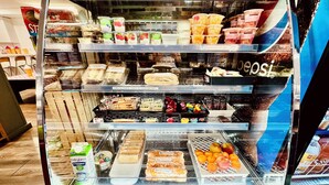 Una vitrina de charcutería con distintos alimentos, como sándwiches, pasteles y productos lácteos.
