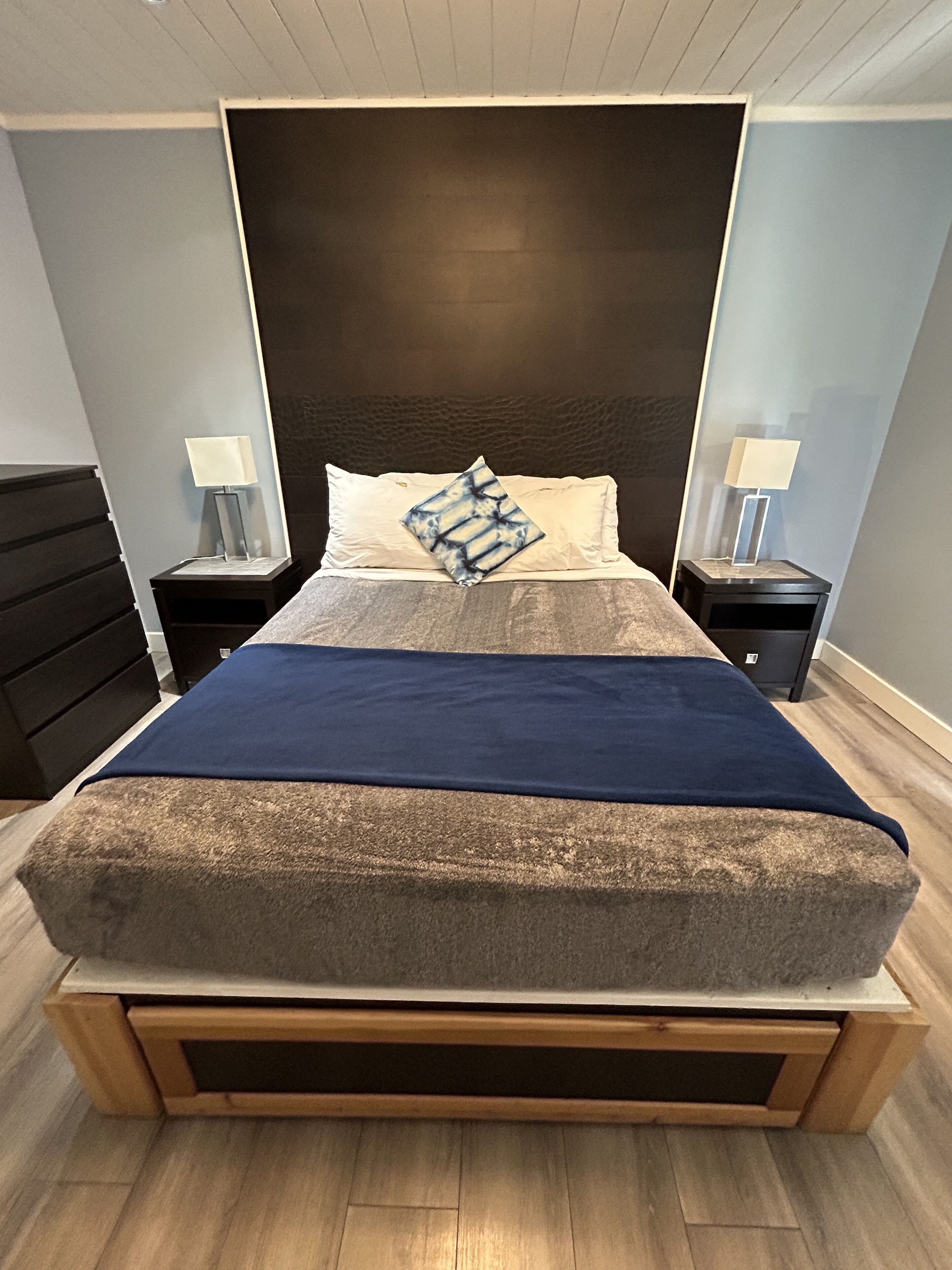 A modern bedroom with a large bed, two nightstands, a dark headboard, and a blue throw blanket.