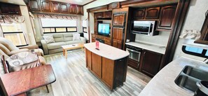 Interior compacto de una caravana con kitchenette, un sofá, una mesita de centro y un televisor.