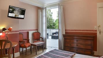 Un dormitorio con cama, cómoda de madera, escritorio con silla y televisor instalado en la pared.