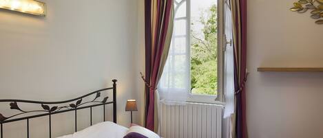 A bedroom with a bed, a window with curtains, a wall-mounted light, and a radiator.