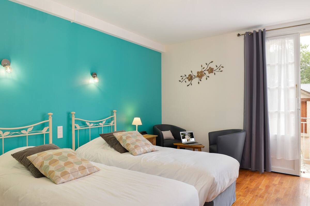 Una habitación de hotel con dos camas, un escritorio, una silla, una lámpara y vistas al exterior.
