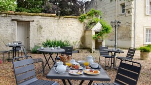 An outdoor café with tables and chairs, a breakfast spread, and a stone wall in the background. - Le Manoir de la Giraudière (Beaumont-en-Veron)