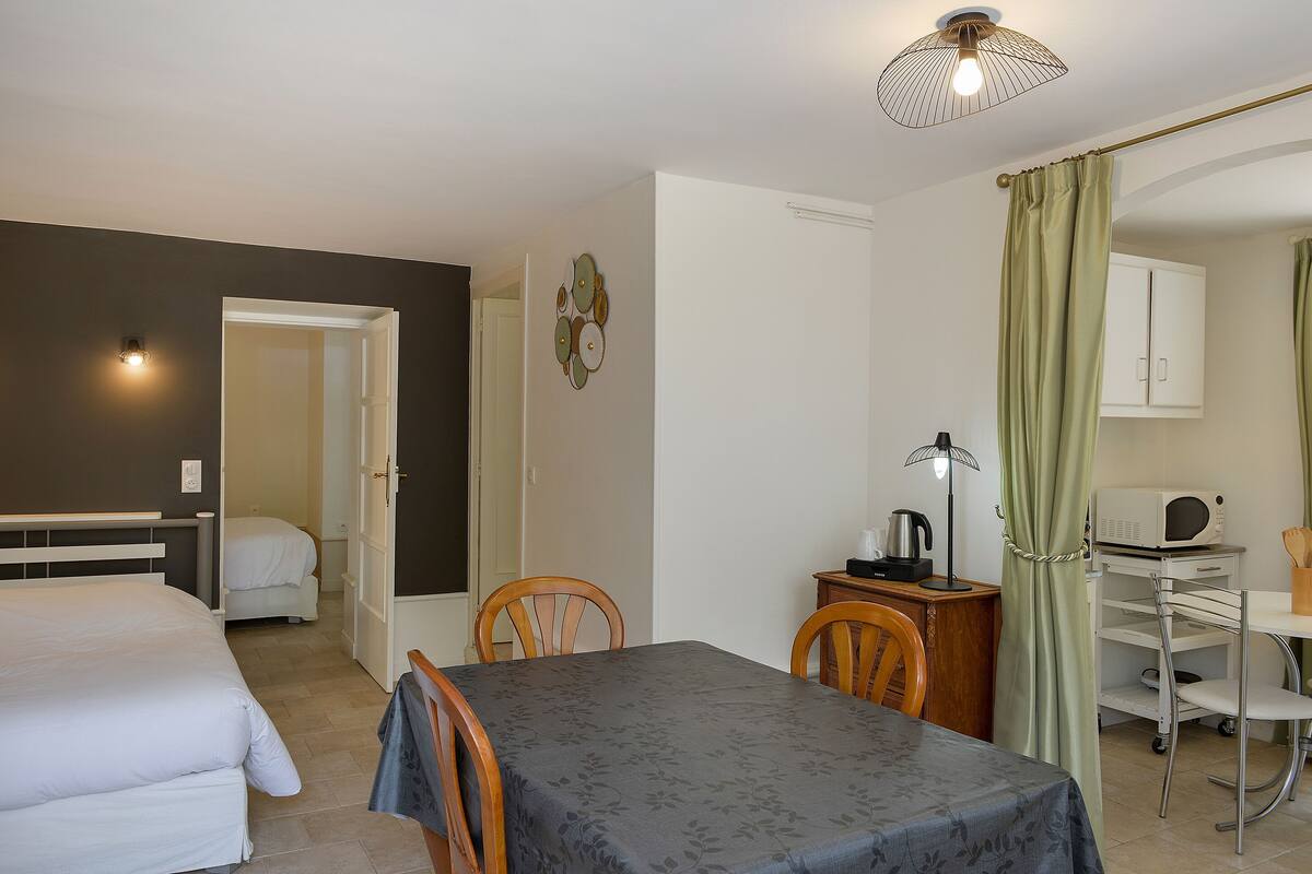 Habitación de hotel con cama, mesa, sillas, escritorio con computadora, microondas y mueble.