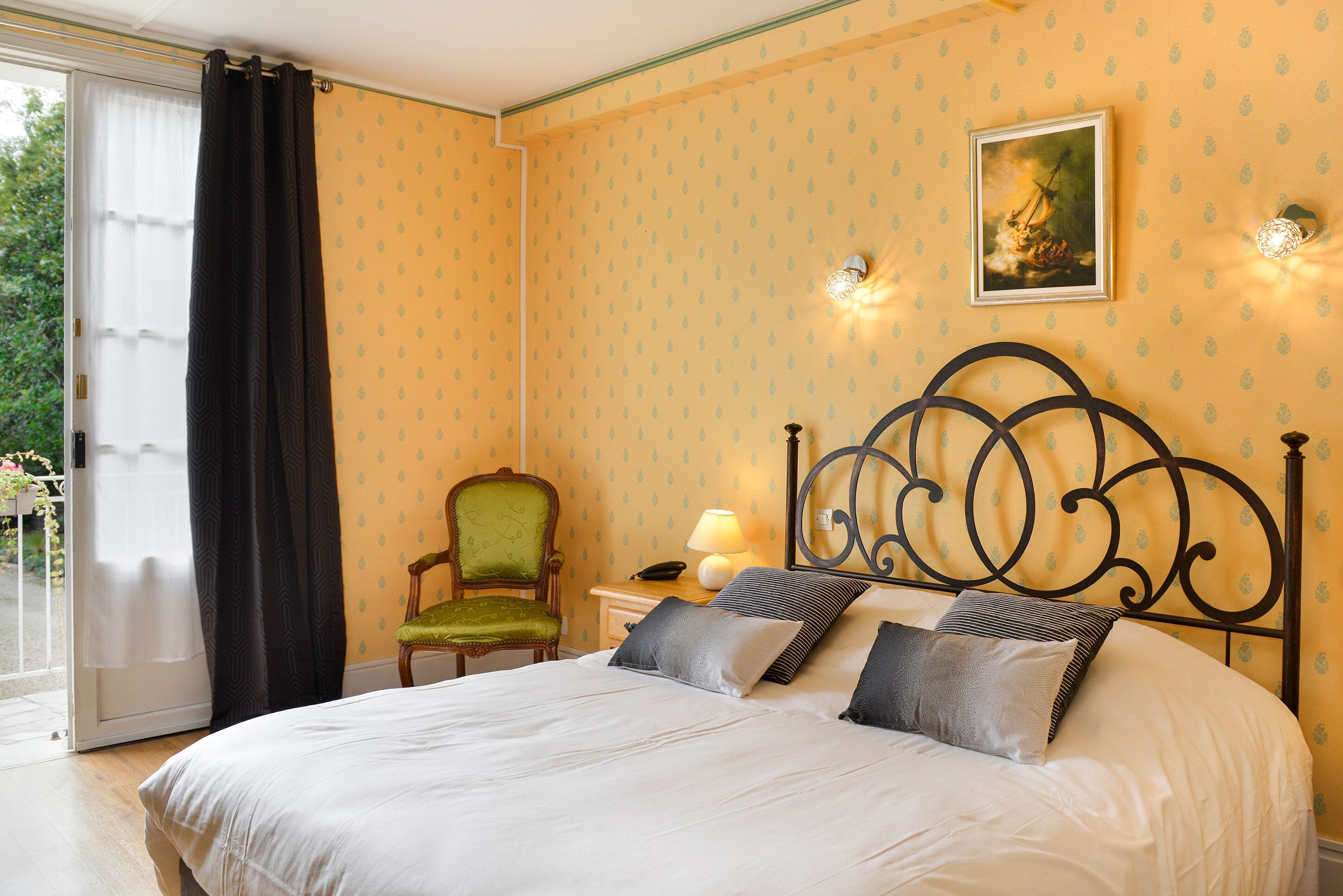 A bedroom with a bed, a chair, a nightstand, and a wall-mounted lamp.