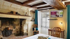 A traditional room with a stone fireplace, a bed with a blue pillow, a wooden chair, and a desk with a lamp. - Le Manoir de la Giraudière (Beaumont-en-Veron)