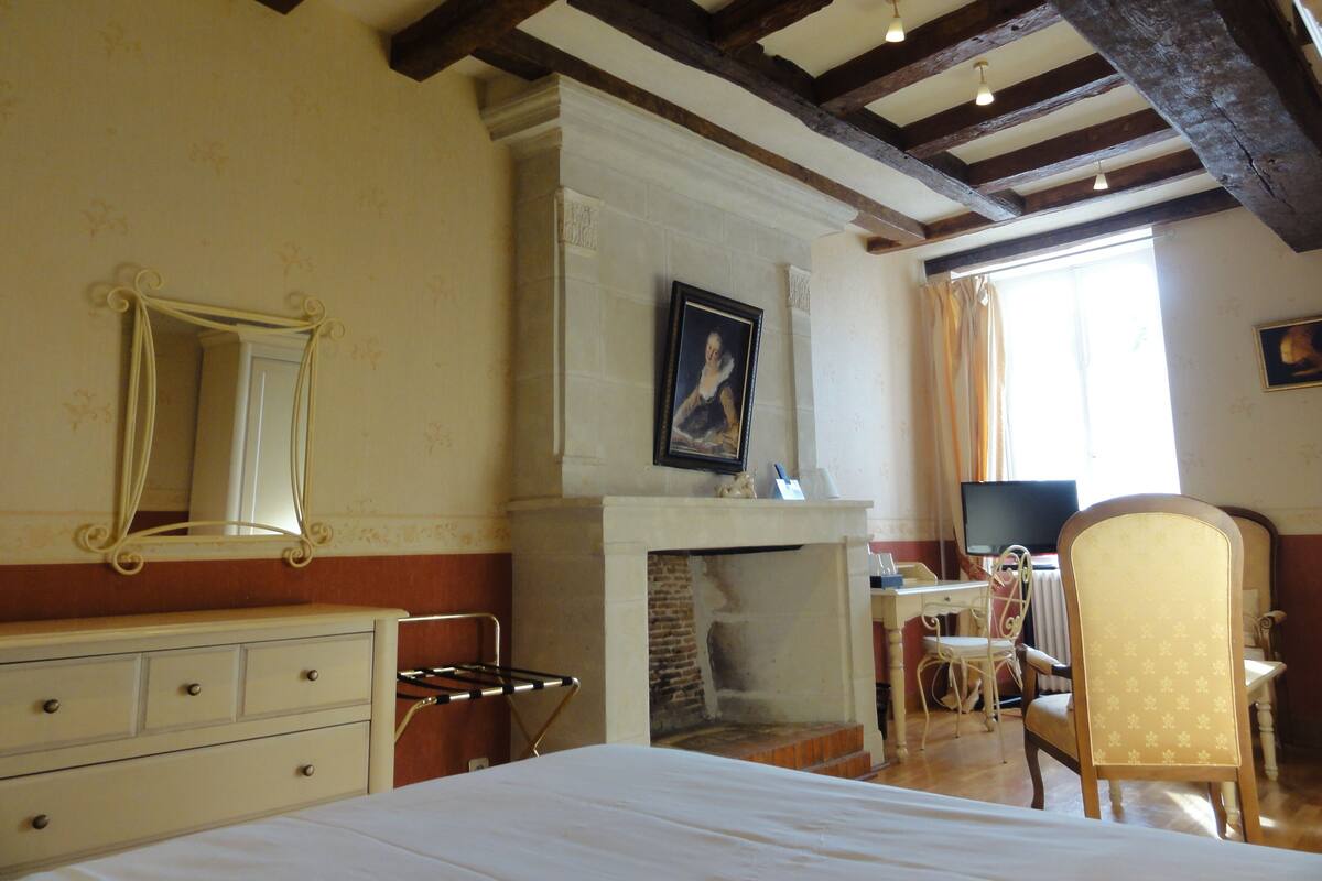 Un dormitorio con cama, cómoda, espejo, chimenea y escritorio con silla.