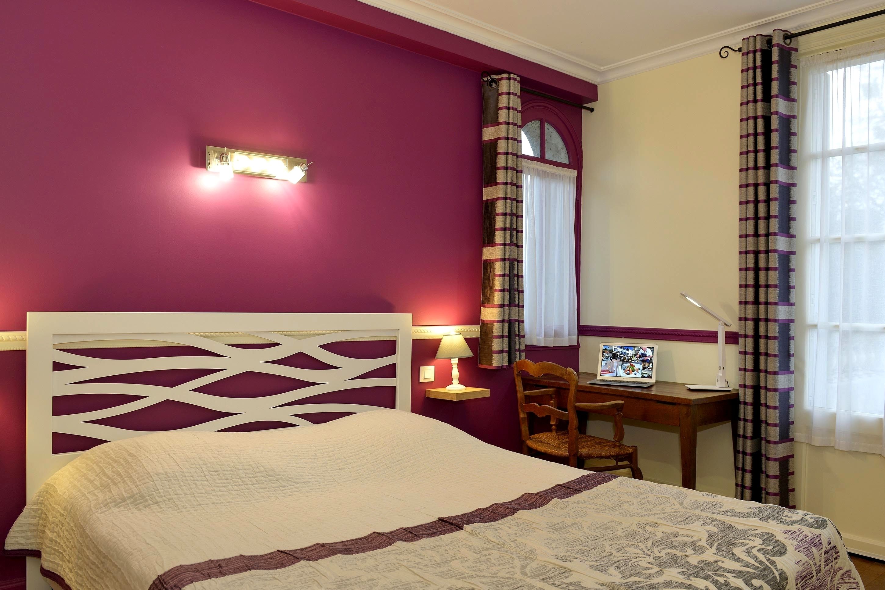A bedroom with a bed, a desk with a computer, a chair, and a window with curtains.