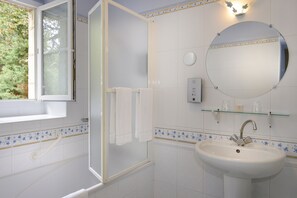 Un baño con ducha, lavamanos, espejo y ventana.