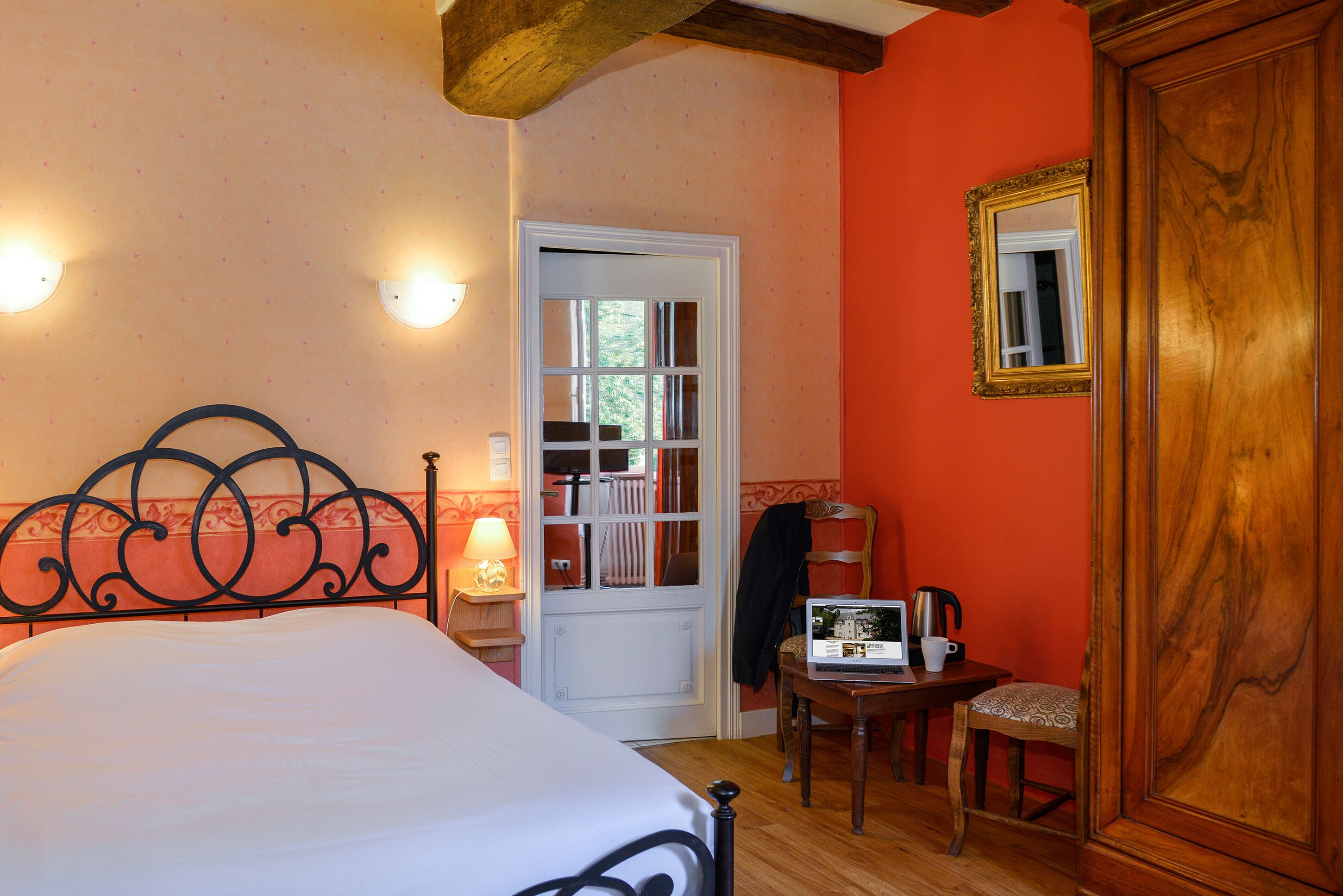 A bedroom with a bed, a wooden door, a small table with a lamp, and a chair.