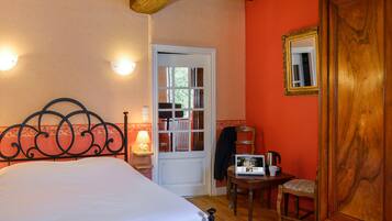 A bedroom with a bed, a wooden door, a small table with a lamp, and a chair.