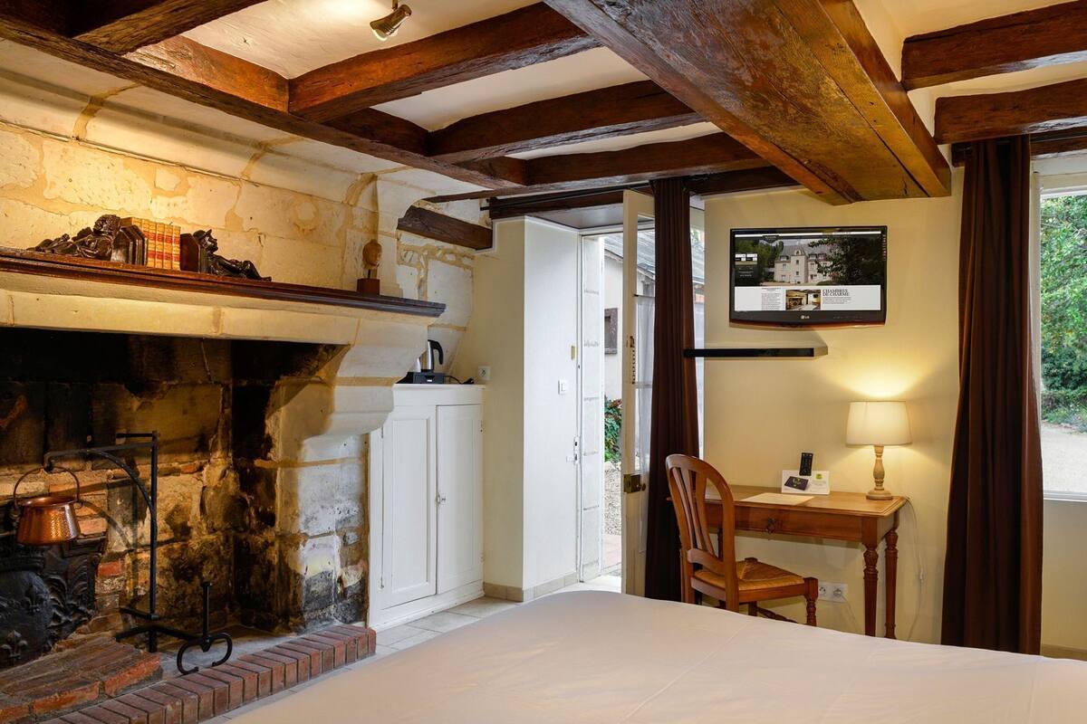 Una habitación con chimenea, un escritorio con lámpara, una cama y una puerta que da al exterior.