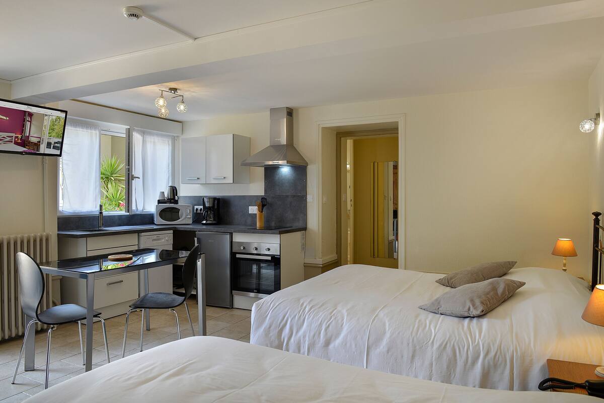 Habitación de hotel compacta con kitchenette, cama con dos almohadas, escritorio con silla y televisor montado en la pared.