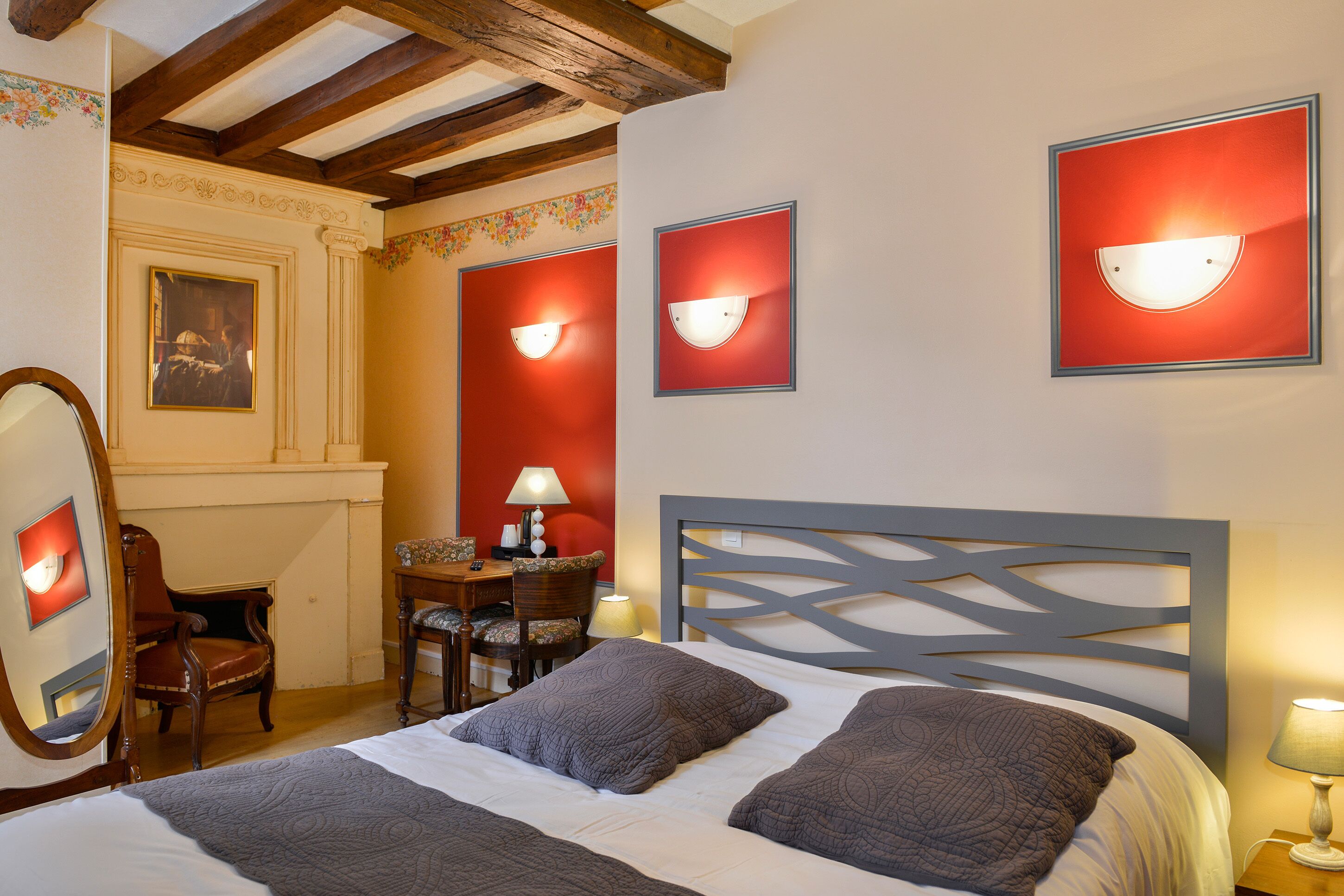 Habitación de hotel con una cama grande, cabecera de madera, un escritorio con silla y una lámpara de pared.
