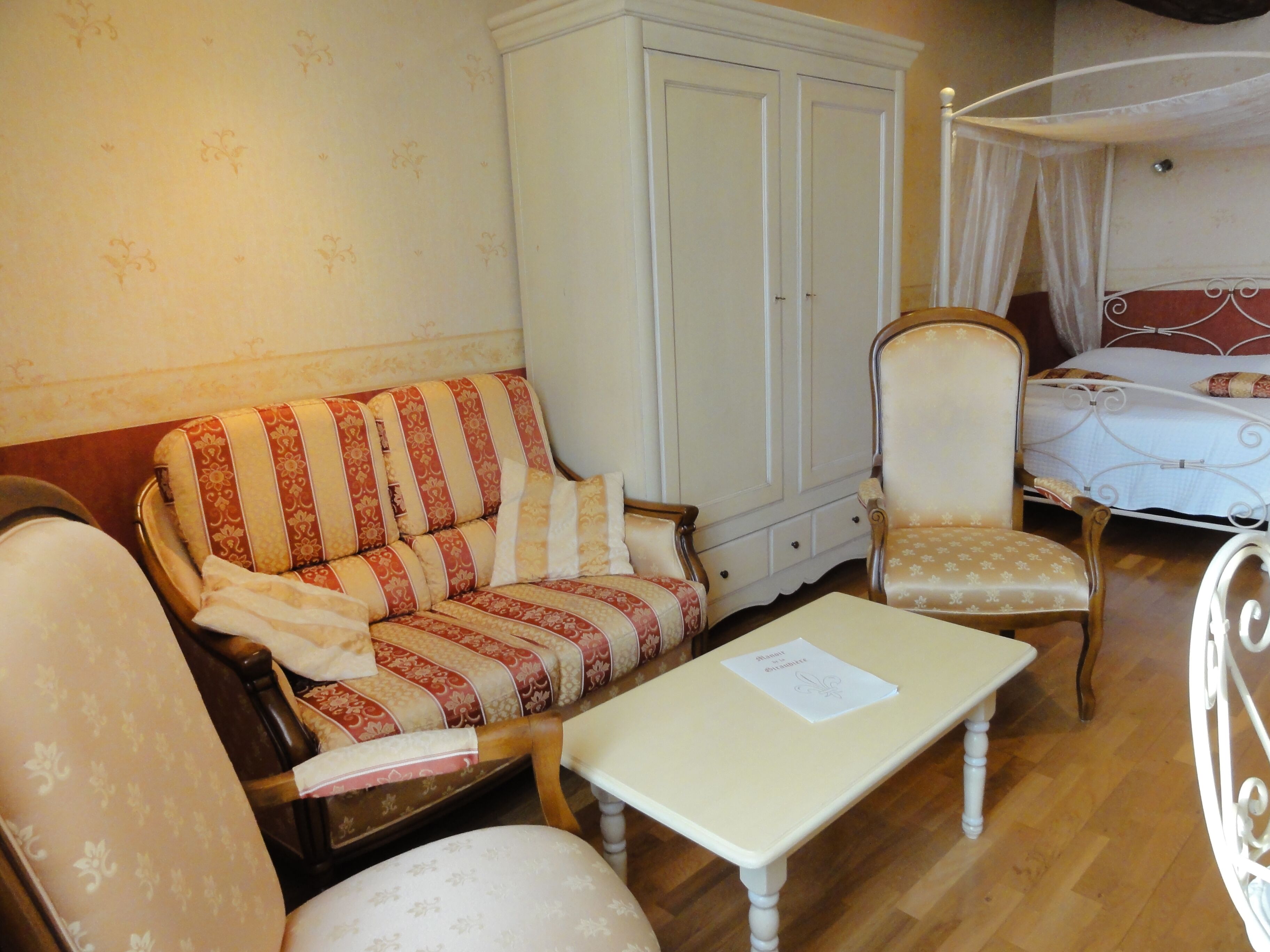 A room with a sofa, a chair, a small table, a wardrobe, and a bed with a canopy.