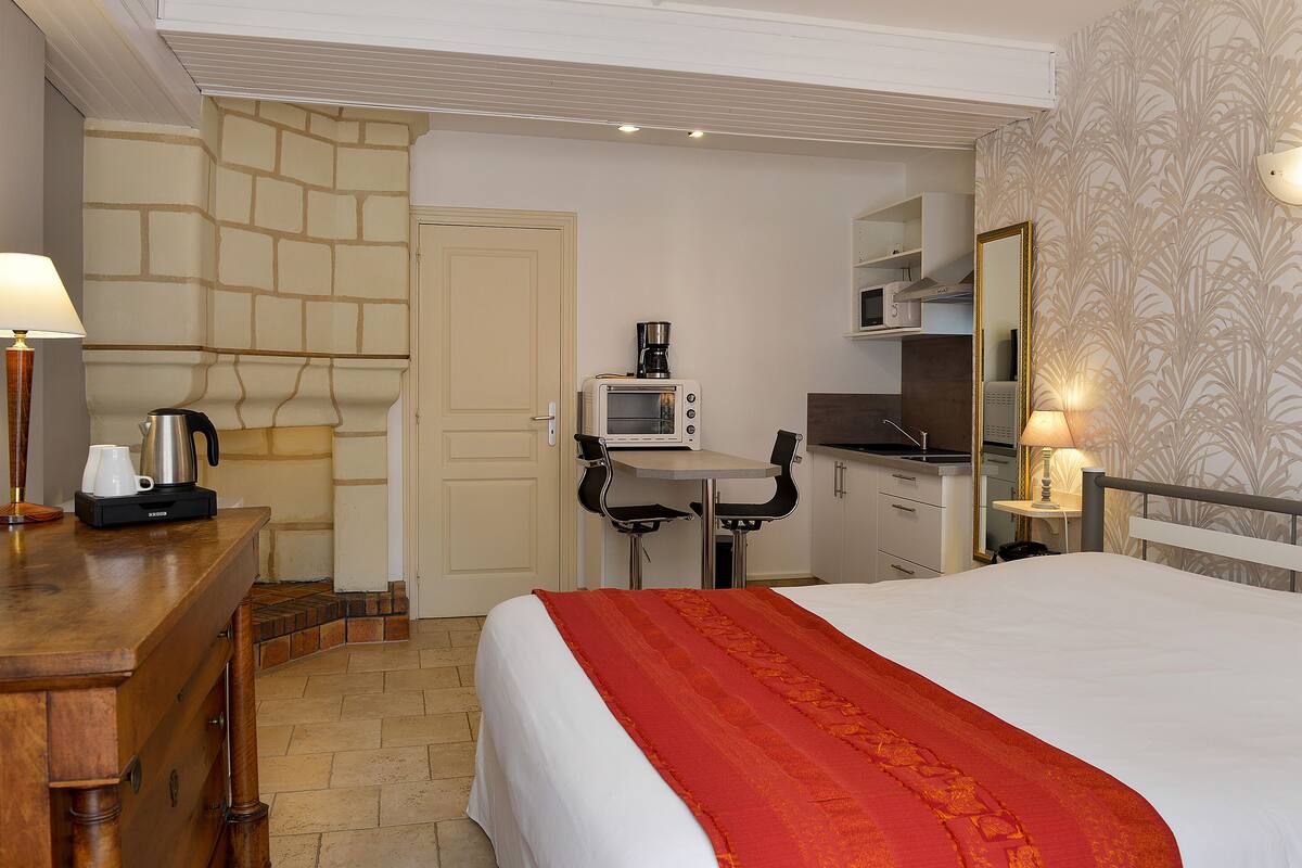Habitación de hotel con cama, escritorio con cafetera, microondas y una pequeña mesa con sillas.