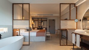 A modern hotel room with a large bathtub, a bed with a wooden headboard, a desk with a chair, and a mirror. - FERGUS Bermudas (Calvia)
