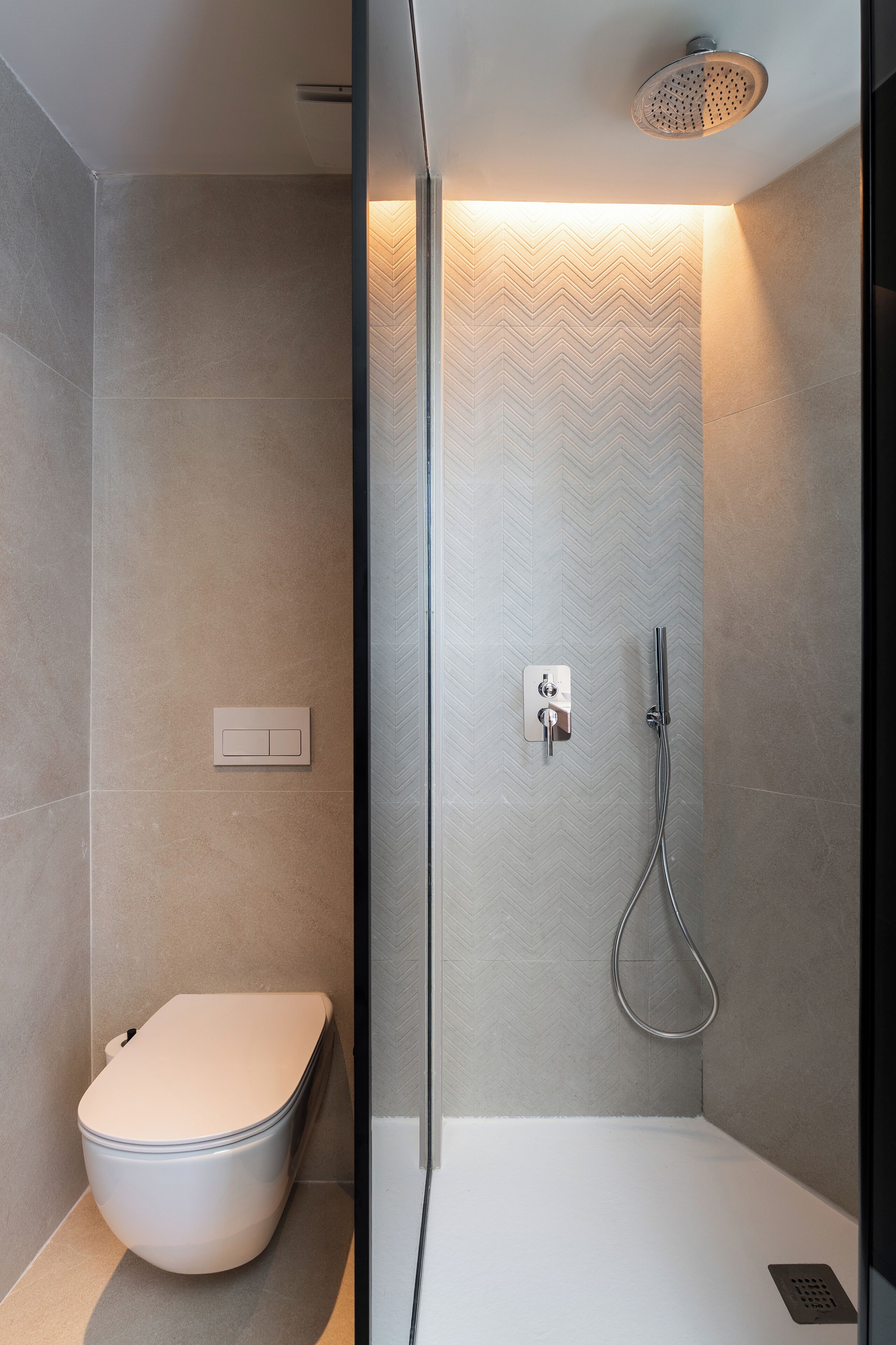 Un baño moderno con ducha, inodoro y pared con patrón de espiga.