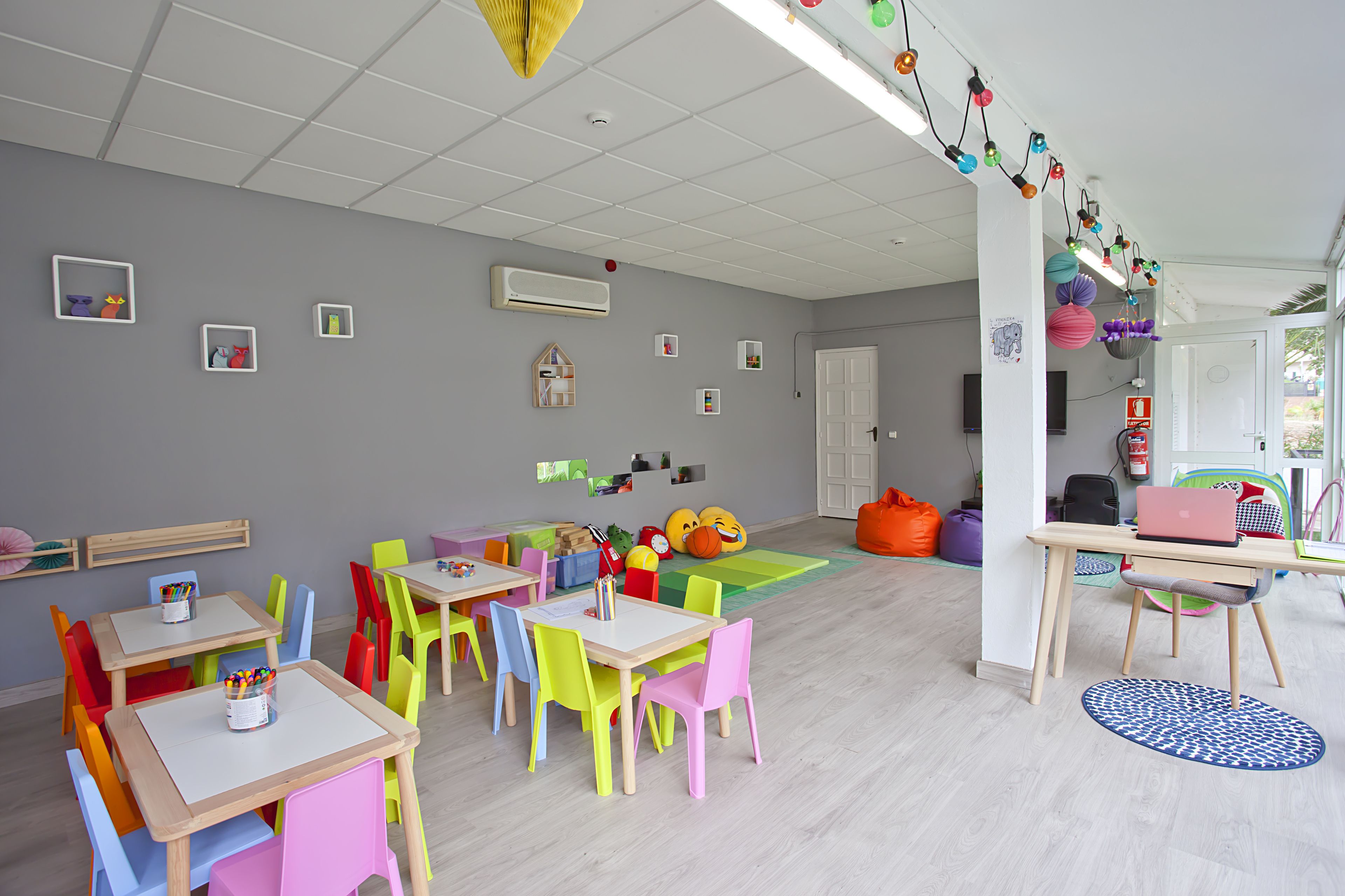 Une salle de jeux pour enfants aux couleurs vives, avec des tables, des chaises et des jouets éducatifs.
