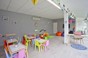 Un salón de juegos infantil, lleno de colores, con mesas, sillas y juguetes educativos.