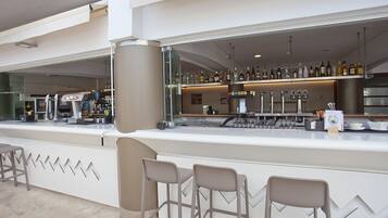 Un área de bar moderna con una barra larga, varios taburetes y una variedad de botellas y vasos a la vista.
