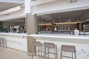 Un área de bar moderna con una barra larga, varios taburetes y una variedad de botellas y vasos a la vista.