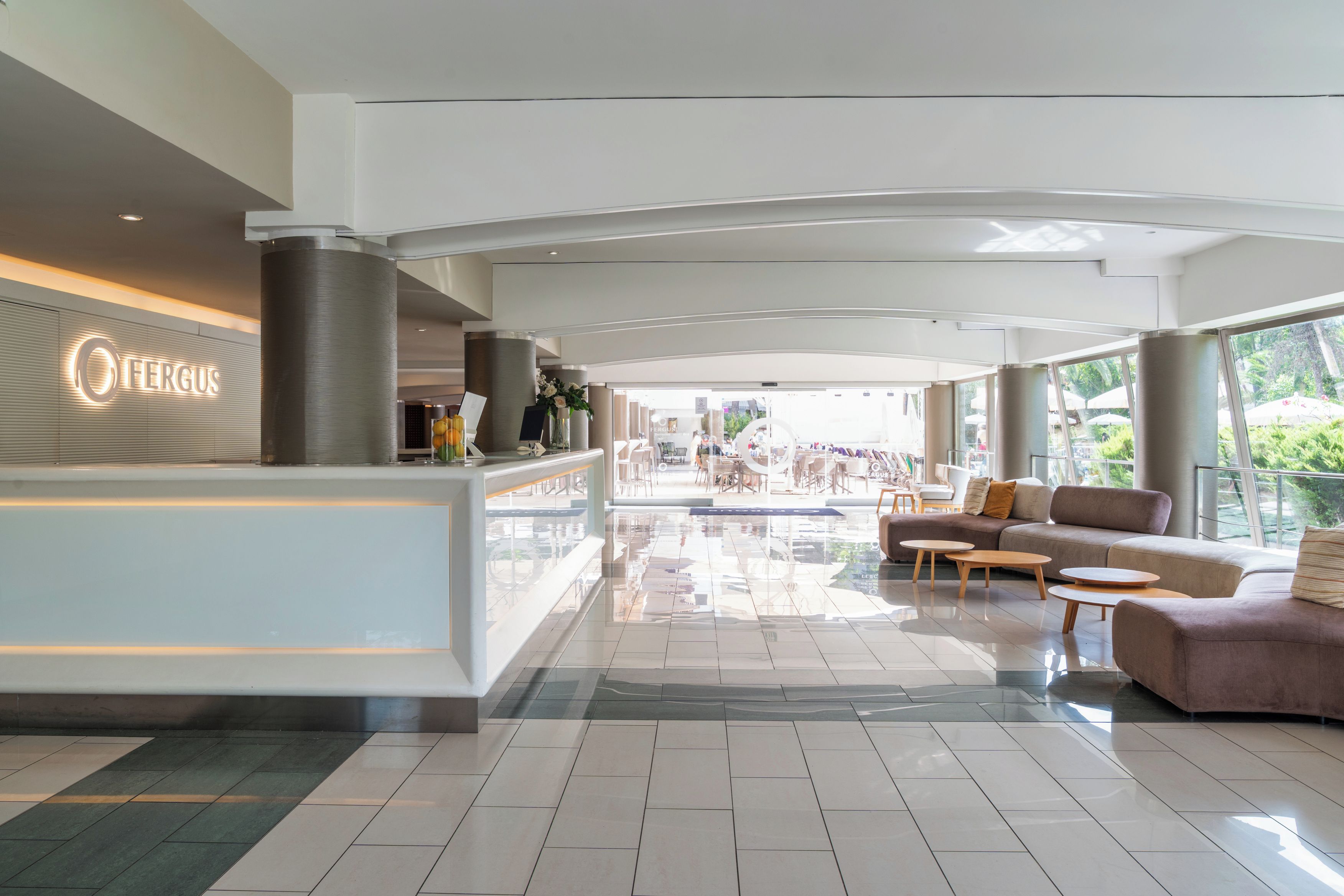 A modern hotel lobby with a reception desk, seating area, and large windows offering a view of the outdoors.