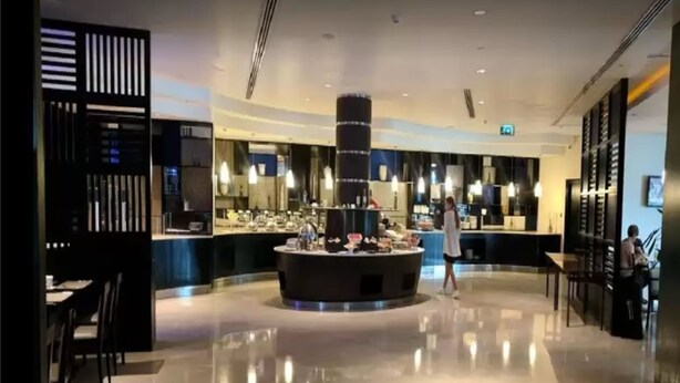 Um lobby de hotel moderno com área circular de bar, espaços para sentar e uma escadaria.