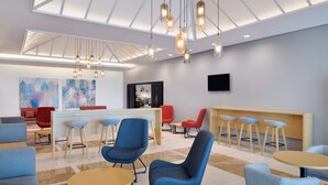 Uma área de estar moderna com cadeiras azuis e cinzentas, mesas de madeira e um bar com bancos.