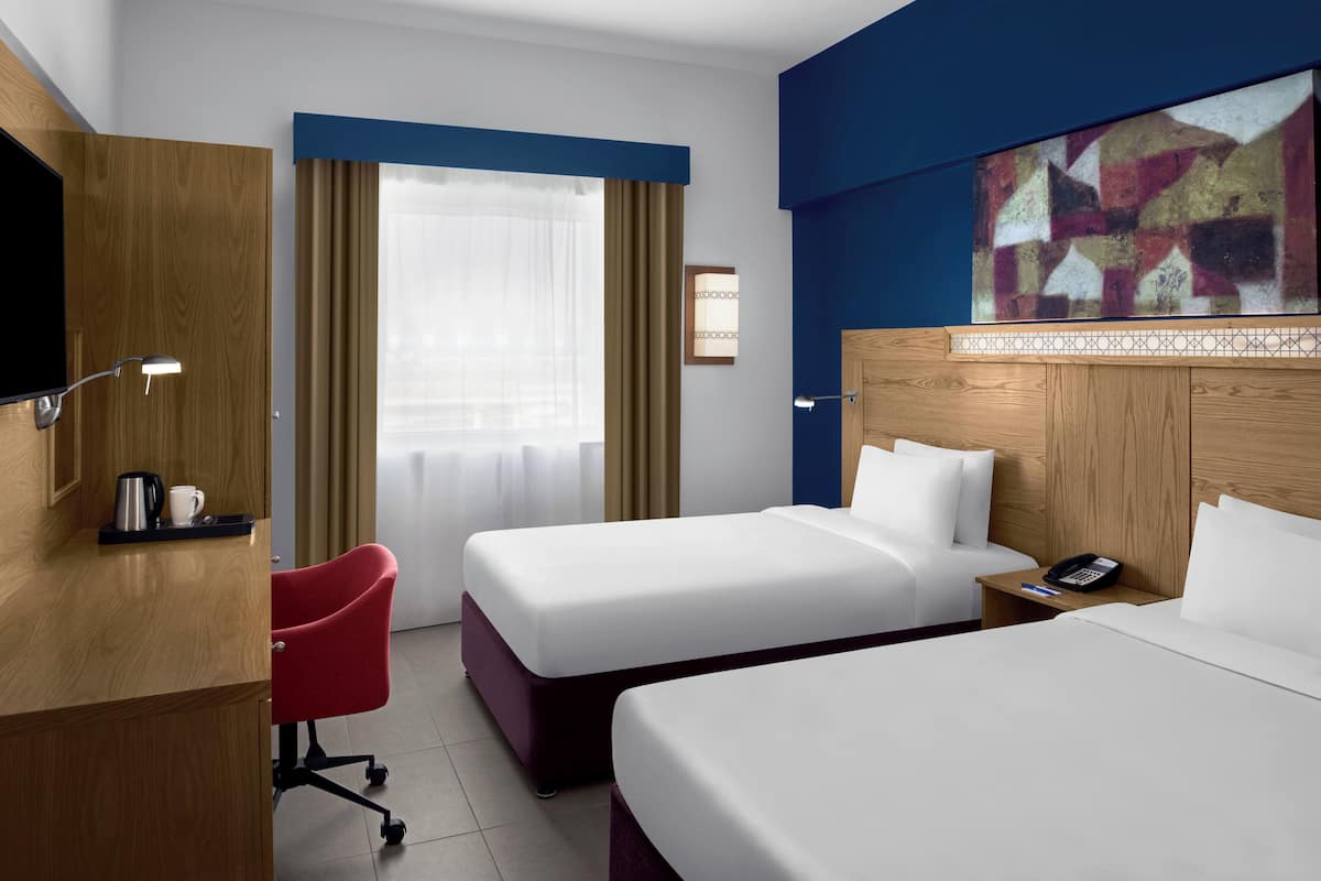 Une chambre d’hôtel avec deux lits, un bureau avec une chaise, une télévision et un tableau au mur.