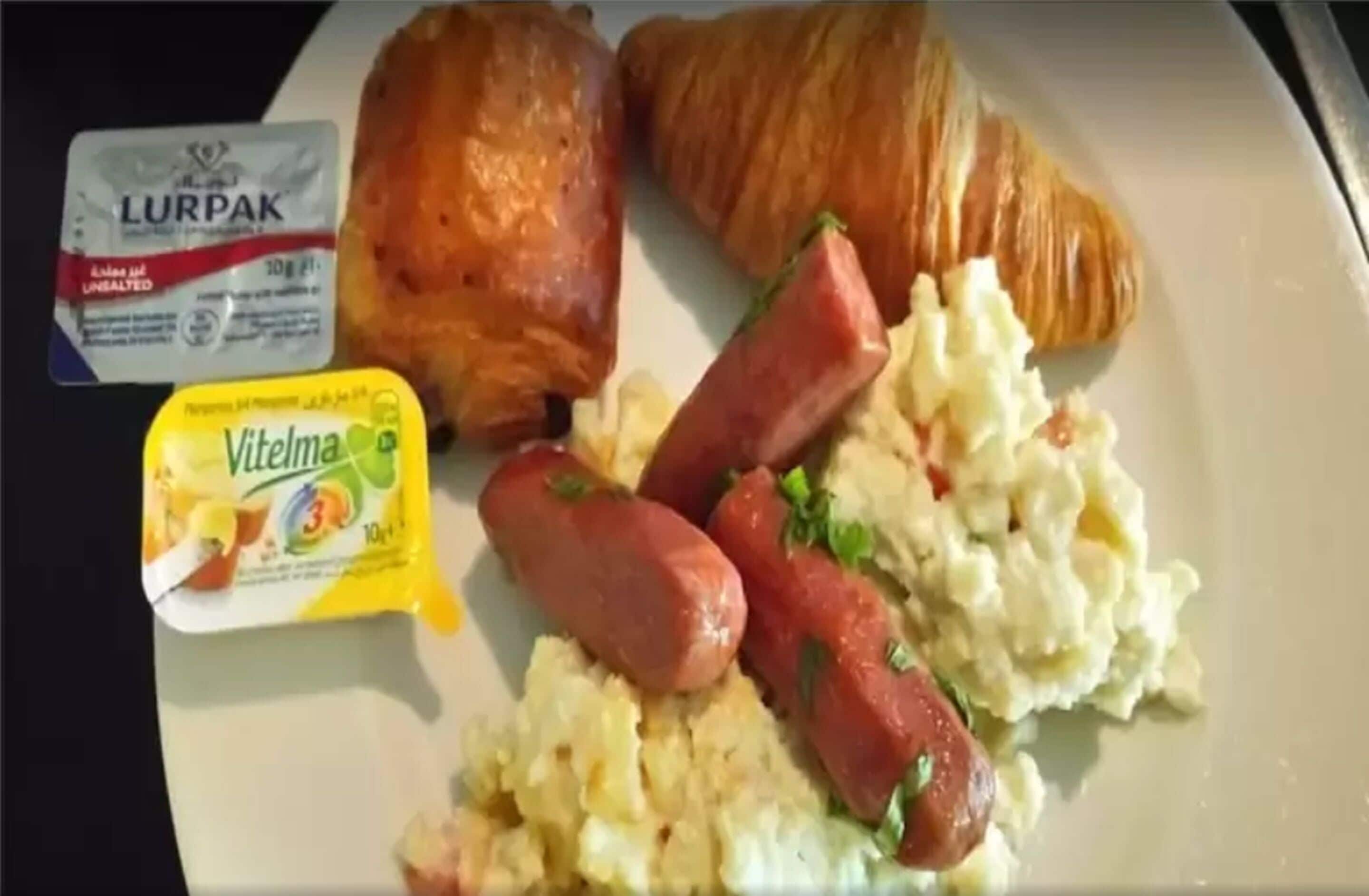 A plate with croissants, sausages, scrambled eggs, and a packet of Lurpak butter.