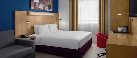 Una habitación de hotel con una cama grande, un escritorio, una silla roja, un sofá, un cuadro en la pared y una ventana con cortinas.