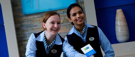 Twee receptiemedewerkers achter de receptiebalie van een Holiday Inn Express, met een bakstenen muur en een grote vaas op de achtergrond.