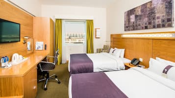 Habitación de hotel con dos camas, un escritorio, un teléfono, un televisor y una ventana con cortinas.