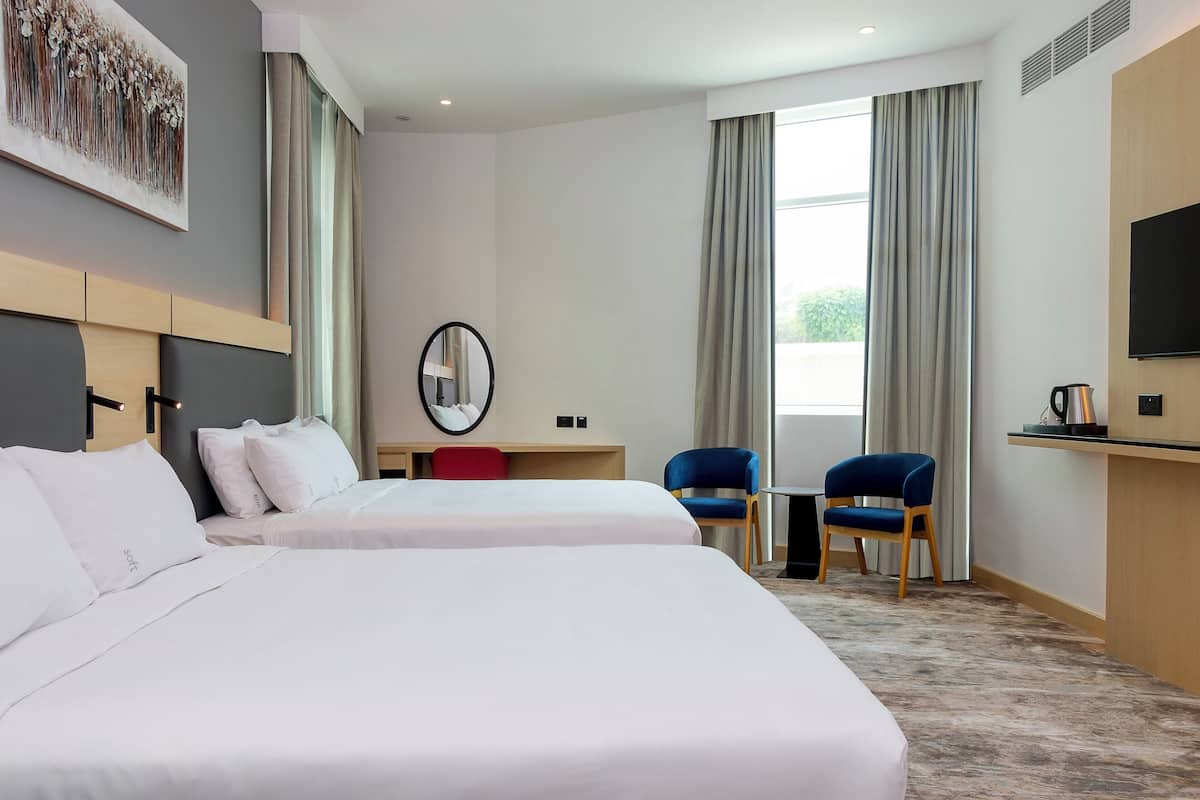Une chambre d’hôtel avec deux lits, un bureau, une chaise, une télévision et une grande fenêtre avec des rideaux.
