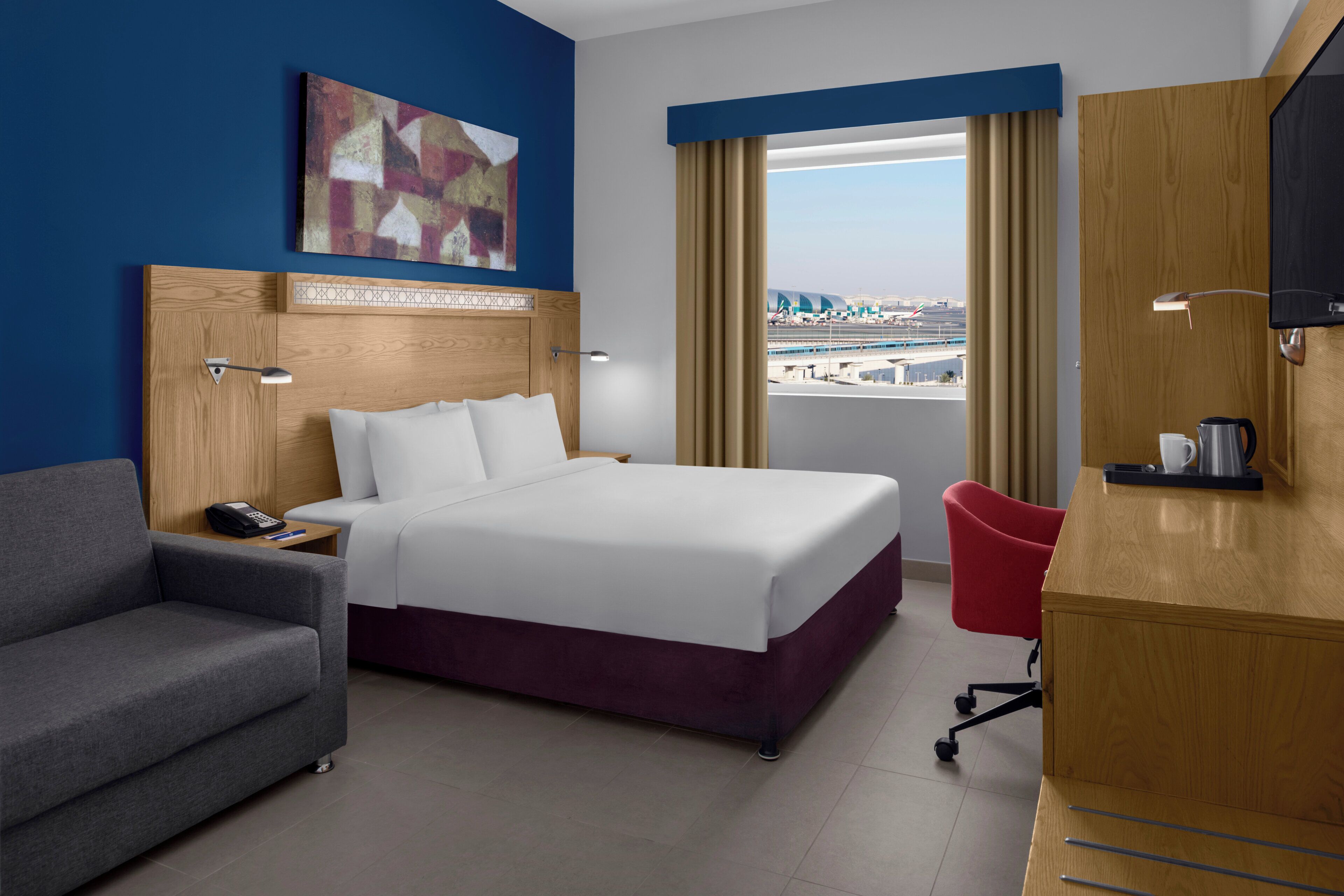 Una camera d'albergo con un letto, una scrivania, una sedia, un telefono e un quadro appeso al muro.