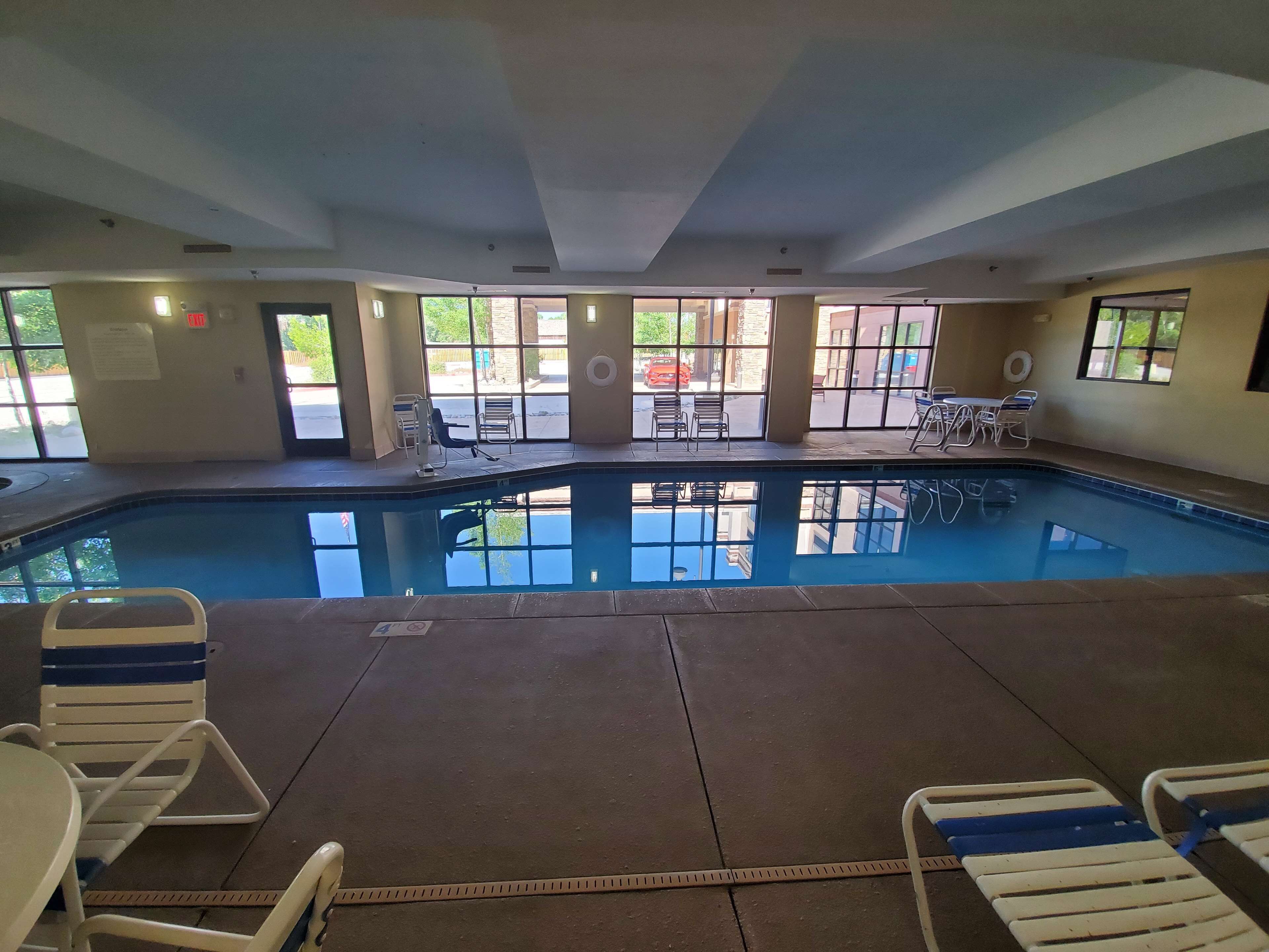 Une piscine intérieure aux parois en verre transparent, entourée de chaises longues et de tables.