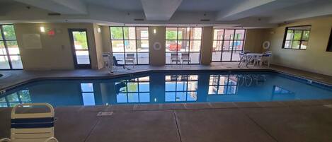 Una piscina interior con paredes de vidrio transparente, rodeada de sillones y mesas.