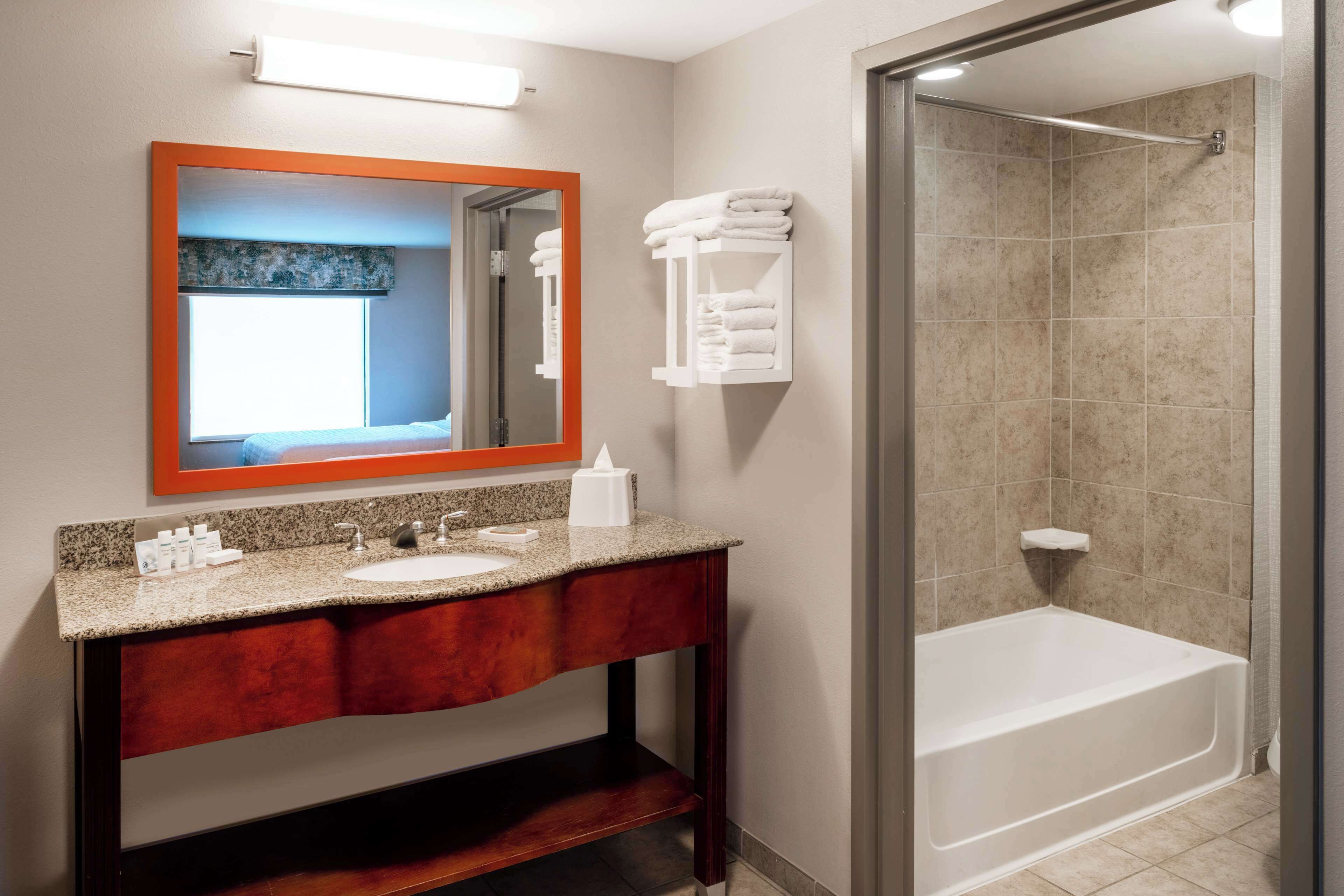 A bathroom with a granite countertop sink, a mirror with an orange frame, and a glass-enclosed shower.