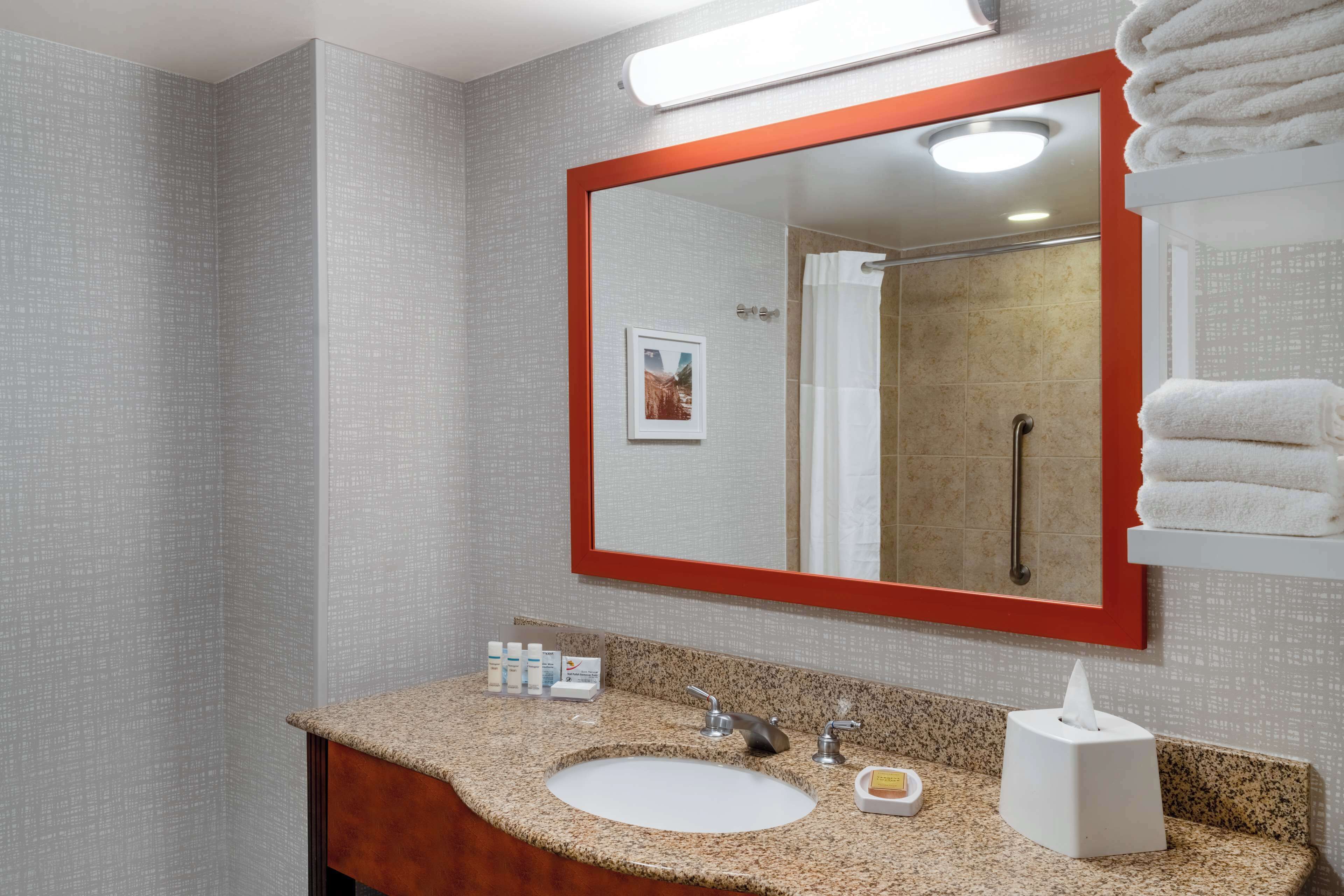 A bathroom with a granite countertop sink, a mirror with a red frame, and a towel rack with folded towels.