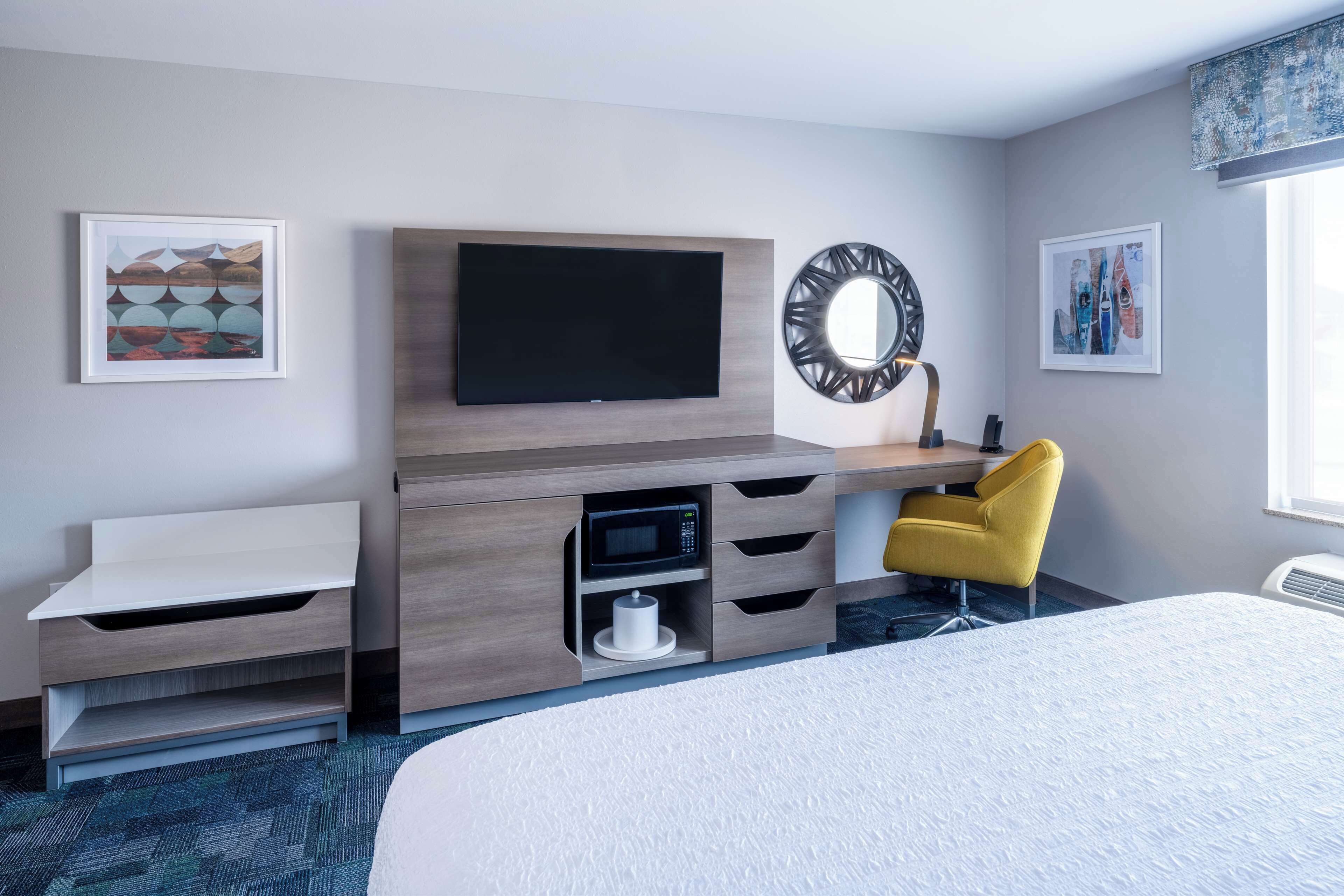 A hotel room with a bed, a desk with a flat-screen TV, a microwave, and a chair.