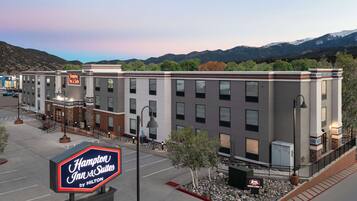 A Hampton Inn & Suites by Hilton hotel with a parking lot, a signboard, and a view of mountains in the background.