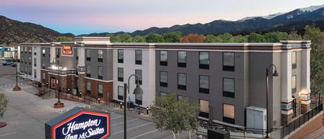 A Hampton Inn & Suites by Hilton hotel with a parking lot, a signboard, and a view of mountains in the background.