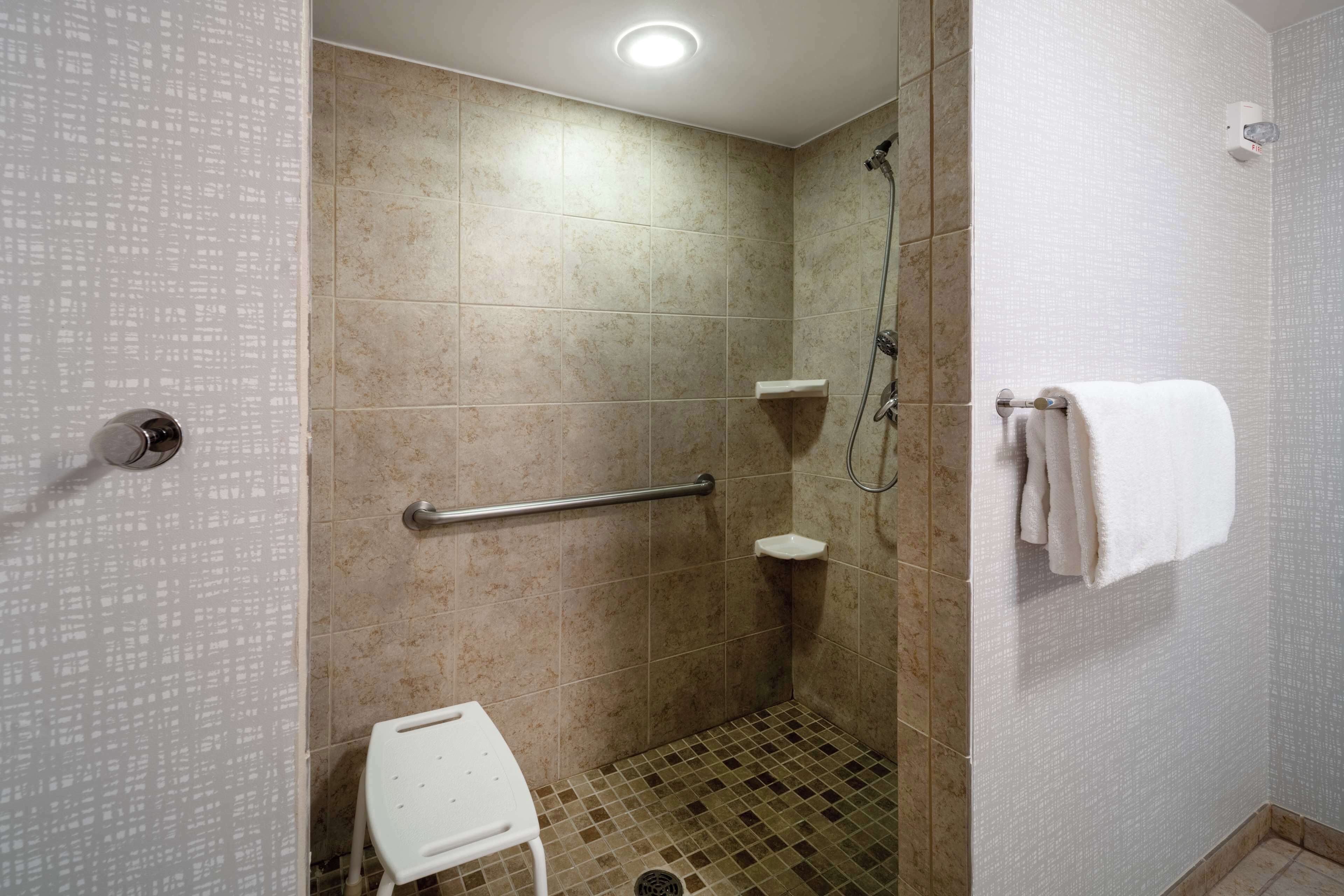 A modern bathroom with beige tiles, a white toilet, a grab bar, a shower area, and a towel rack.