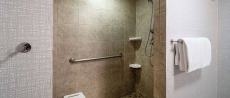 A modern bathroom with beige tiles, a white toilet, a grab bar, a shower area, and a towel rack.