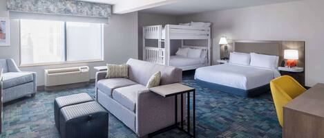 A hotel room with a bunk bed, a sofa, a desk, and a chair.