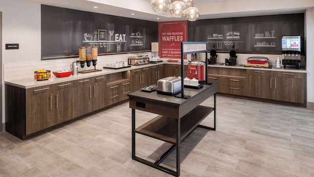 A modern kitchen with a central island, a chalkboard wall, and a waffle station.